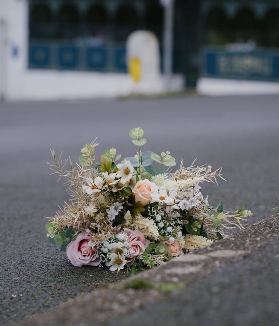A delicate floral bouquet resting on an outdoor pavement, featuring pale pink roses, white daisies, and small sprigs of eucalyptus with round leaves, arranged with soft greenery and wispy, dried eleme